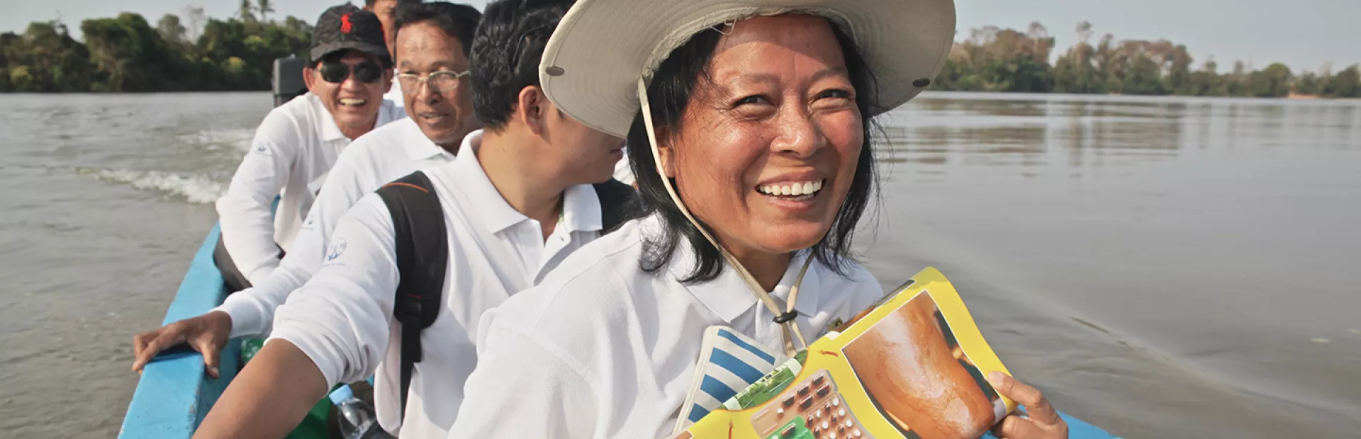 Image of people in a boat in Cambodia holding poster with information about treatment of leprosy