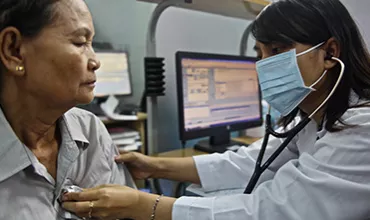 Physician wearing a mask, with a stethoscope listening to a female patient's heart