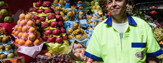 Image of a fruit seller standing in front of a fruit stand